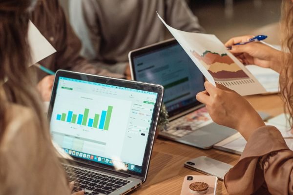 A group engaged in a business meeting analyzing charts on laptops and papers.